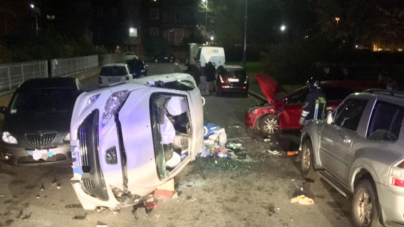 Auto carambola su mezzi parcheggiati e si ribalta